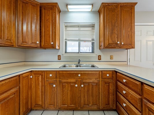 kitchen with brown cabinetry, light tile patterned floors, light countertops, and a sink