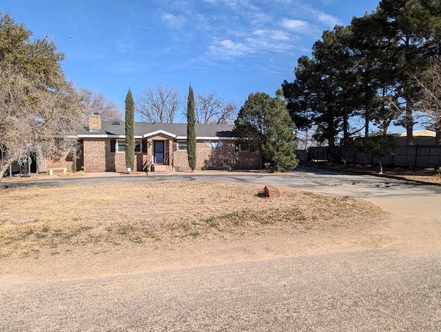 ranch-style home with brick siding, a chimney, and fence