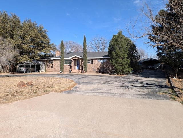 ranch-style home with aphalt driveway, a chimney, brick siding, and a carport