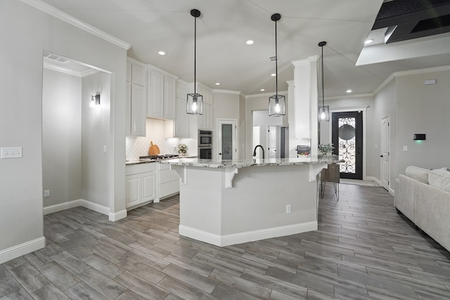 kitchen featuring a breakfast bar, white cabinetry, pendant lighting, light stone countertops, and decorative backsplash