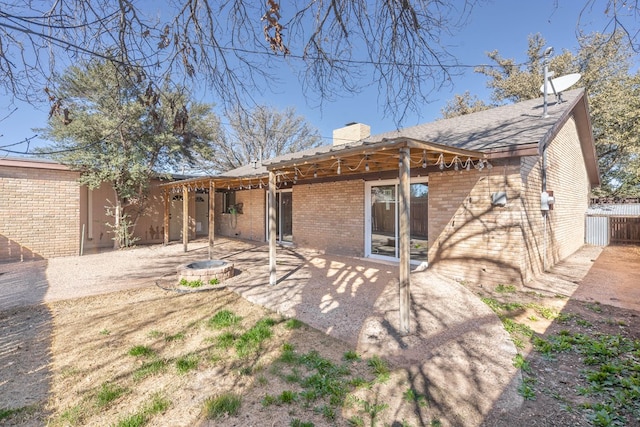 rear view of property with an outdoor fire pit, brick siding, fence, a chimney, and a patio area