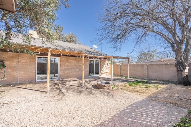 back of house with brick siding, fence, a fire pit, and a patio