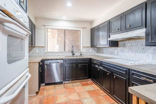 kitchen with under cabinet range hood, white appliances, a sink, light countertops, and dark cabinetry