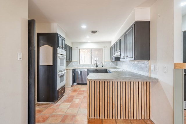 kitchen with visible vents, a peninsula, stainless steel dishwasher, under cabinet range hood, and backsplash