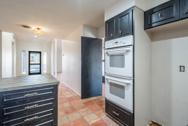 kitchen featuring double oven, light countertops, visible vents, and dark cabinetry