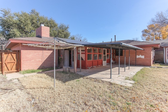 rear view of property with a sunroom, solar panels, a patio area, and a yard