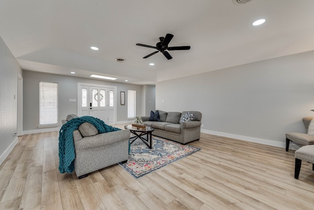 living area with light wood-type flooring, baseboards, ceiling fan, a tray ceiling, and recessed lighting