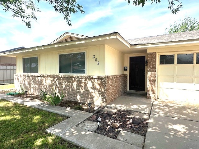 view of exterior entry with an attached garage and brick siding