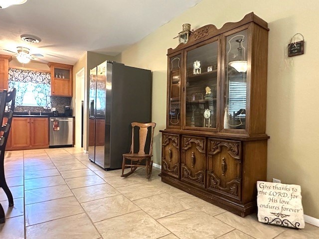 kitchen with stainless steel appliances, dark countertops, a ceiling fan, decorative backsplash, and glass insert cabinets