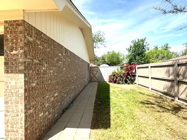 view of side of property with brick siding, a yard, fence, and a gate