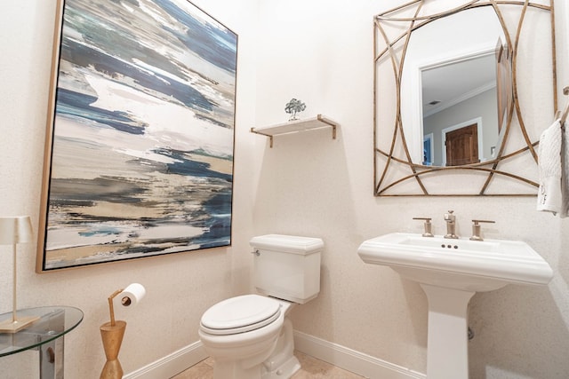 half bath with baseboards, toilet, tile patterned floors, crown molding, and a sink