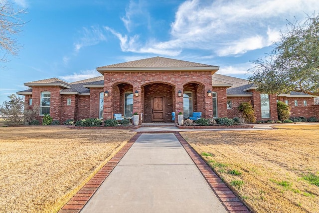 view of front of property featuring a shingled roof, brick siding, and a front lawn