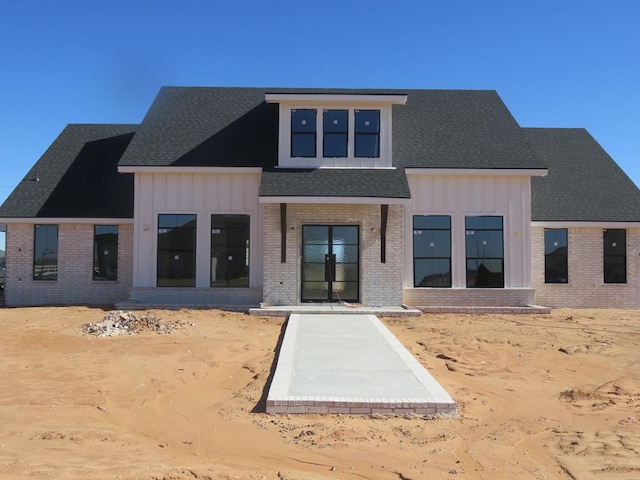 rear view of property featuring brick siding, a shingled roof, and board and batten siding
