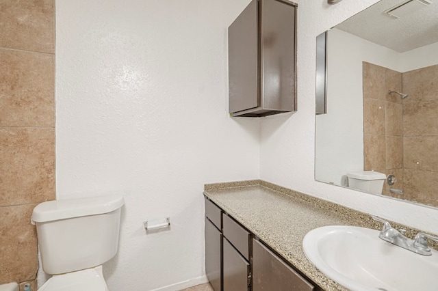 bathroom featuring vanity, tiled shower, a textured ceiling, and toilet