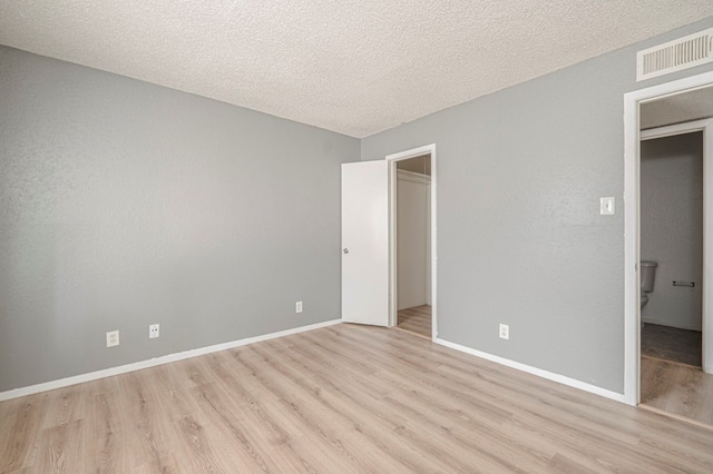 unfurnished bedroom with a closet, a walk in closet, light hardwood / wood-style floors, and a textured ceiling