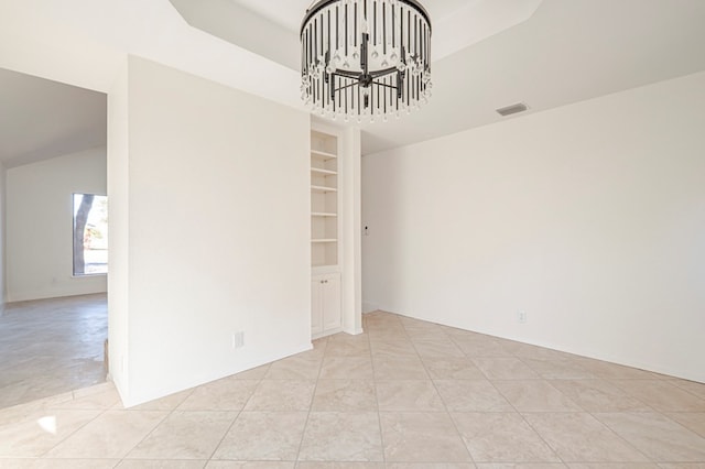 empty room featuring a chandelier, light tile patterned floors, built in features, and a raised ceiling