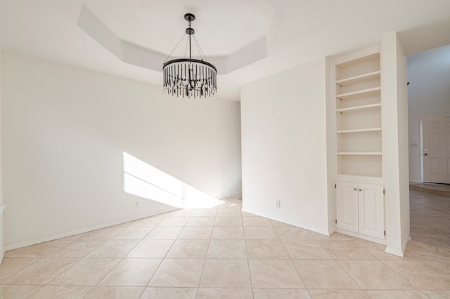 tiled spare room with built in shelves, an inviting chandelier, and a tray ceiling