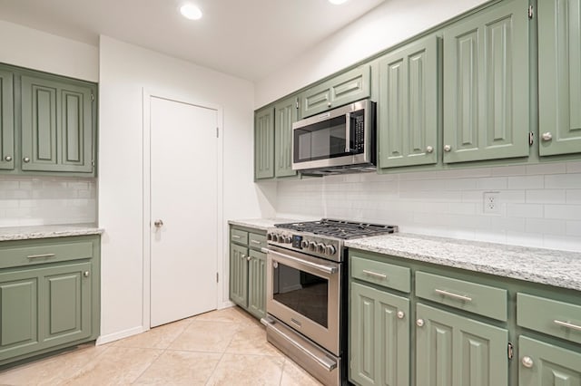 kitchen with green cabinets, decorative backsplash, appliances with stainless steel finishes, light tile patterned flooring, and light stone counters