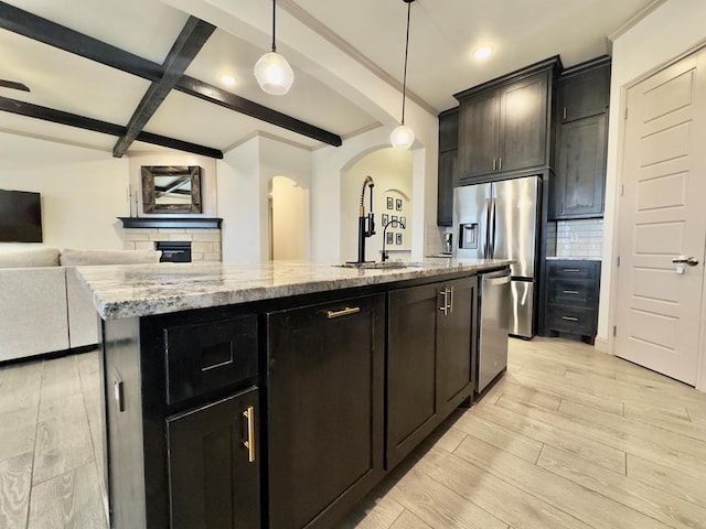 kitchen with hanging light fixtures, stainless steel appliances, tasteful backsplash, a center island with sink, and light wood-type flooring