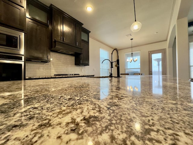 kitchen with light stone countertops, a chandelier, pendant lighting, dark brown cabinets, and appliances with stainless steel finishes