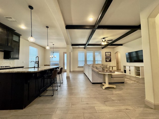 living room featuring light wood-type flooring, ceiling fan with notable chandelier, a wealth of natural light, and beamed ceiling