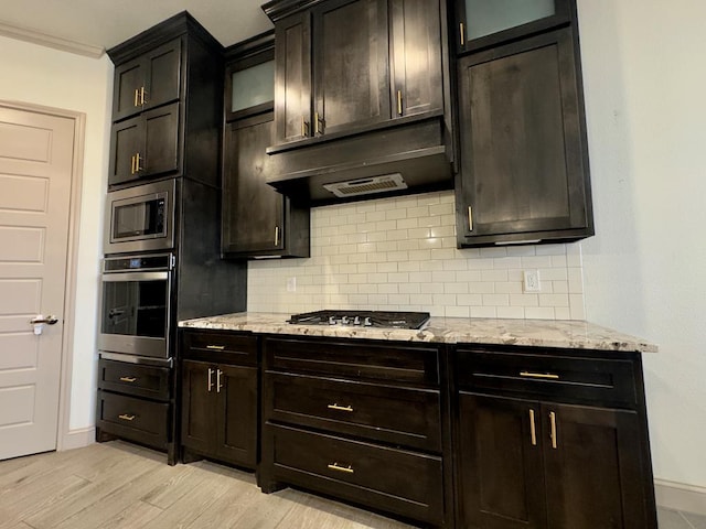 kitchen featuring backsplash, crown molding, light stone countertops, light hardwood / wood-style floors, and stainless steel appliances