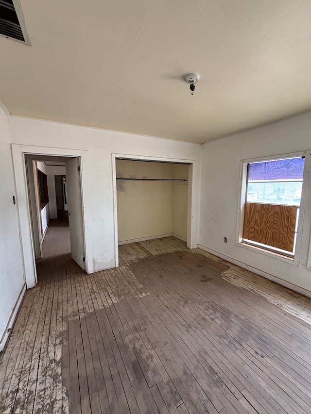 unfurnished bedroom with baseboards, hardwood / wood-style floors, visible vents, and a closet