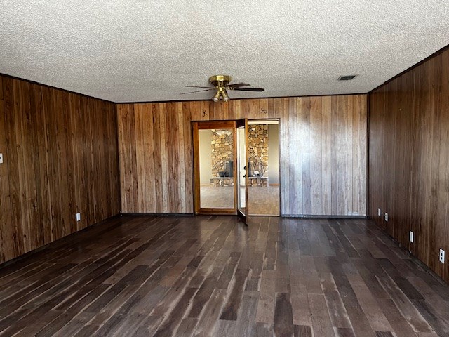 spare room featuring ceiling fan, wooden walls, a textured ceiling, and dark hardwood / wood-style floors