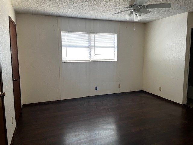 empty room with ceiling fan, dark wood-type flooring, and a textured ceiling