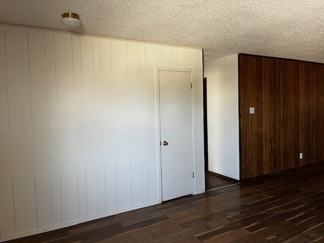 empty room featuring a textured ceiling, dark hardwood / wood-style flooring, and wood walls