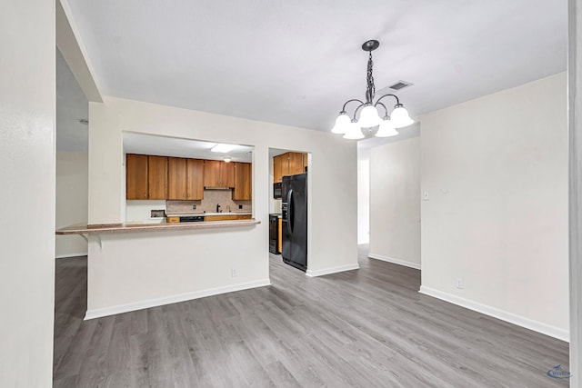 3404 W Michigan Ave, Midland, TX 79703 - kitchen with black fridge, brown cabinetry, wood finished floors, a chandelier, and a sink