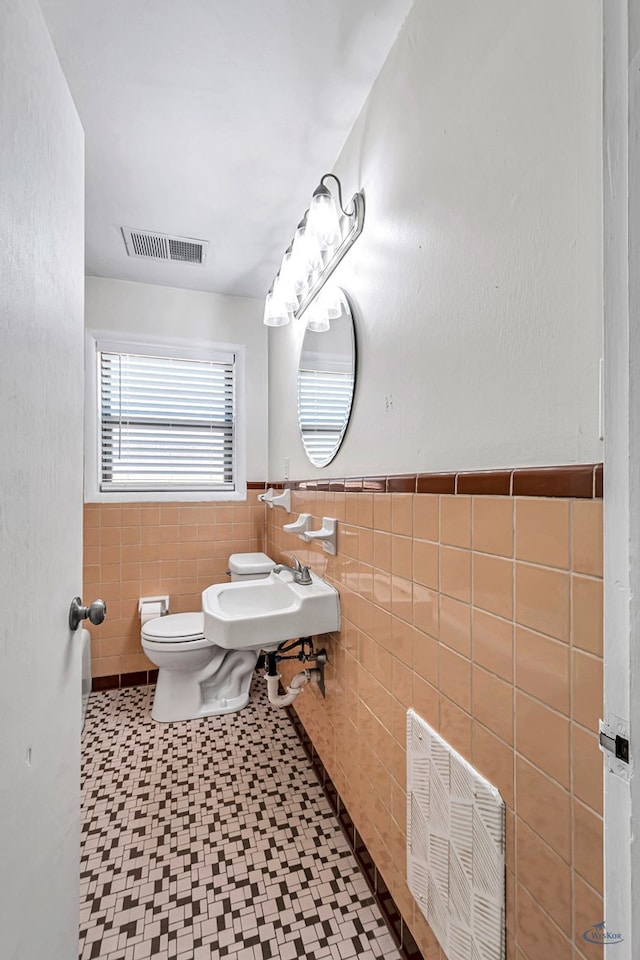 3404 W Michigan Ave, Midland, TX 79703 - bathroom with tile walls, tile patterned floors, toilet, a wainscoted wall, and a sink