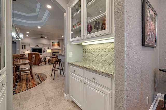 kitchen with white cabinetry, light stone countertops, a tray ceiling, decorative backsplash, and light tile patterned flooring