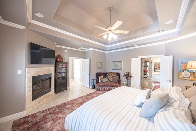 tiled bedroom with a tray ceiling, ceiling fan, ornamental molding, and a tiled fireplace