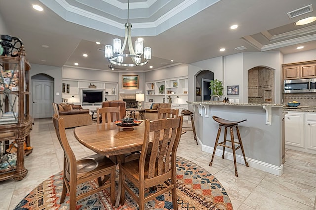 dining room with a raised ceiling, built in features, crown molding, and a chandelier