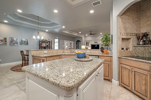 kitchen with ceiling fan with notable chandelier, a raised ceiling, sink, a large island, and light stone counters