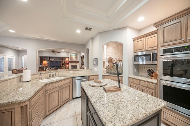 kitchen with light stone countertops, sink, a center island, a tray ceiling, and appliances with stainless steel finishes