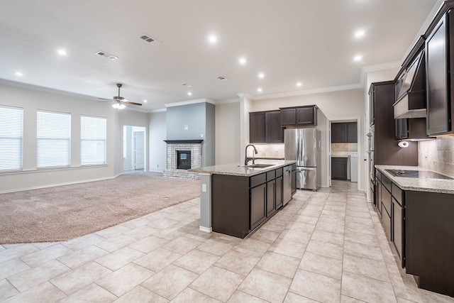 kitchen with an island with sink, tasteful backsplash, sink, stainless steel refrigerator, and light colored carpet