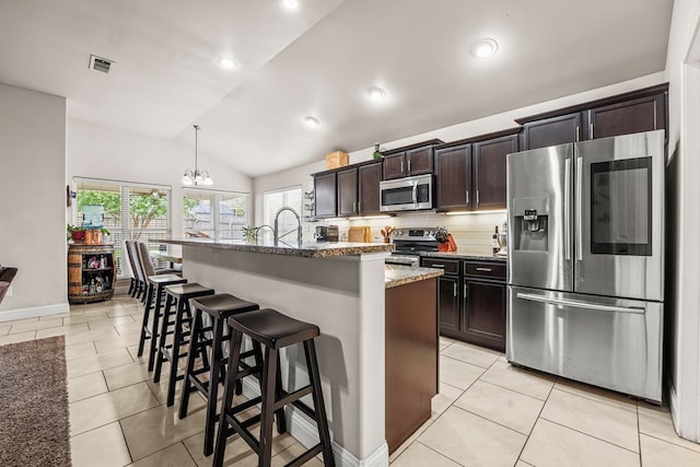 9910 Aloe Ct, Odessa, TX 79765 - kitchen featuring stainless steel appliances, a center island with sink, light tile patterned flooring, a breakfast bar area, and vaulted ceiling
