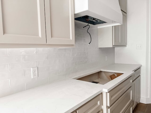 kitchen with light stone countertops, decorative backsplash, premium range hood, and dark hardwood / wood-style floors