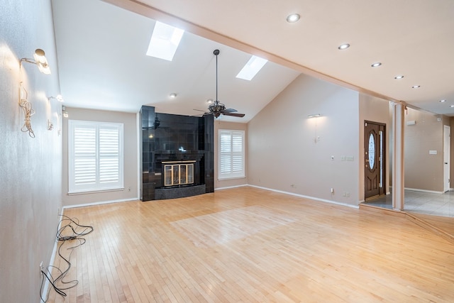 unfurnished living room featuring a skylight, high vaulted ceiling, ceiling fan, a fireplace, and light hardwood / wood-style floors