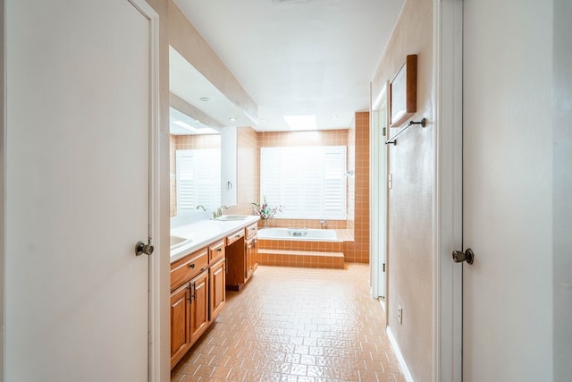 bathroom with a relaxing tiled tub, plenty of natural light, and vanity