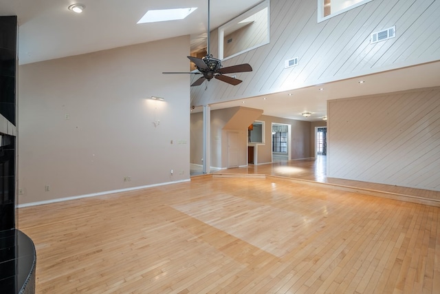unfurnished living room with a skylight, high vaulted ceiling, light hardwood / wood-style floors, and ceiling fan