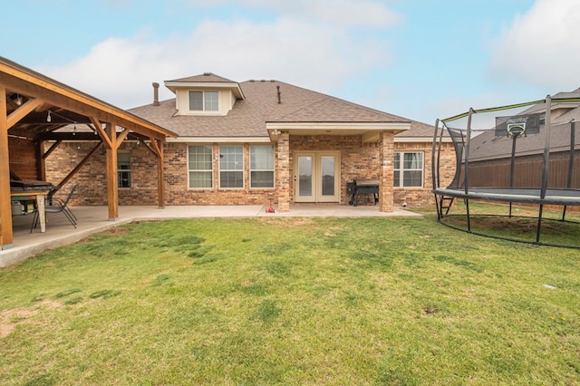 back of house featuring a patio area, brick siding, roof with shingles, and a trampoline