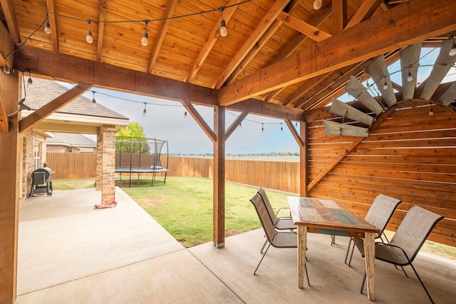 view of patio with a trampoline, outdoor dining space, and a fenced backyard