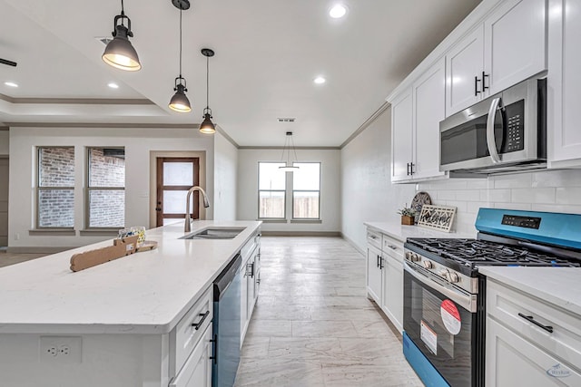 kitchen with appliances with stainless steel finishes, decorative light fixtures, white cabinetry, sink, and a center island with sink