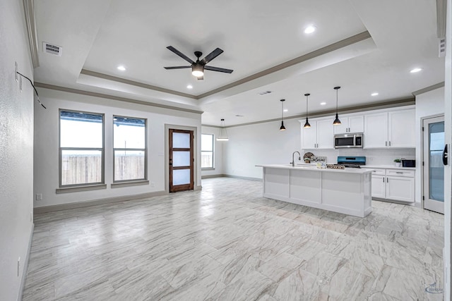 kitchen with white cabinetry, decorative light fixtures, a raised ceiling, stainless steel appliances, and a kitchen island with sink