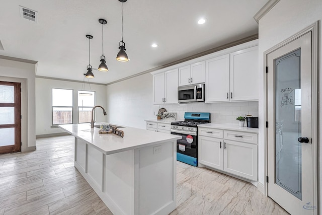 kitchen with appliances with stainless steel finishes, decorative light fixtures, an island with sink, and white cabinets