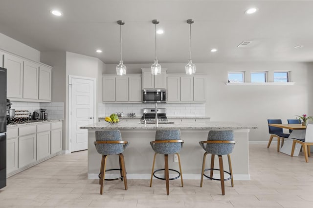 kitchen featuring an island with sink, a breakfast bar area, light stone countertops, stainless steel appliances, and a sink