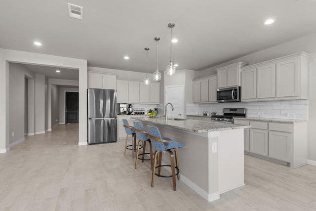 kitchen featuring a breakfast bar, visible vents, appliances with stainless steel finishes, a sink, and an island with sink